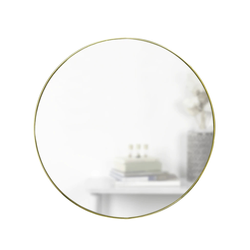 A HUBBA MIRROR 86cm BRASS, manufactured by Umbra, sitting on a table next to a vase.