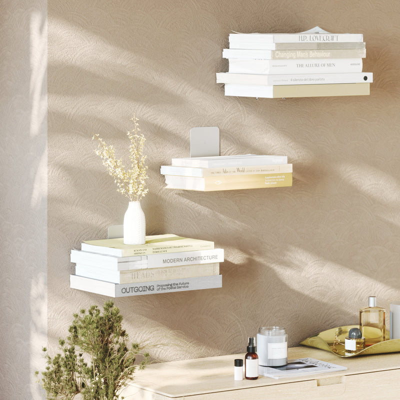 A minimalist white floating shelf with books and a vase, perfect for space-saving, the Umbra Conceal 3 Pack - Silver.