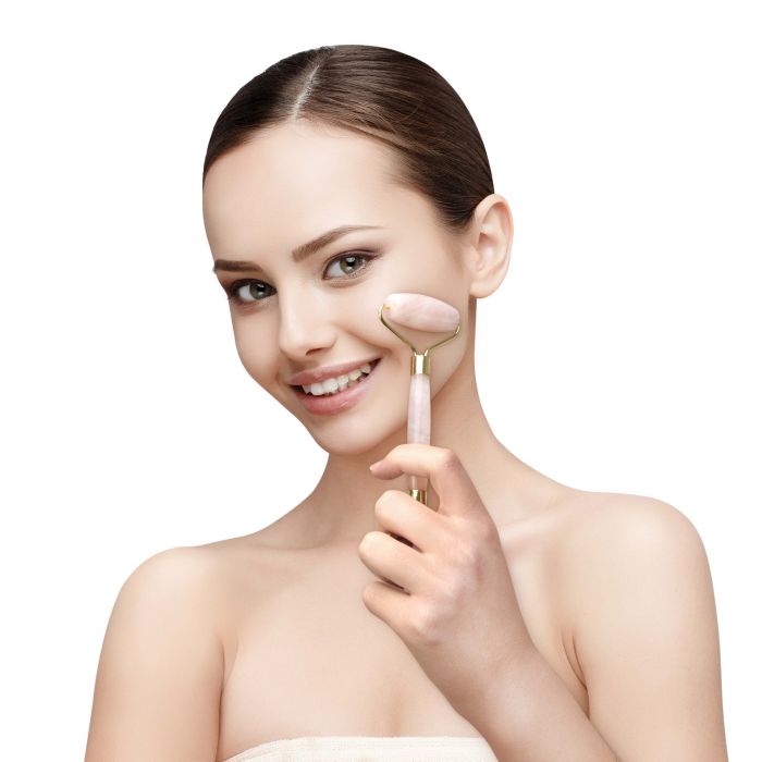 A woman with a radiant skin tone is holding a Crystal Facial Roller from Albi, smiling as she revitalizes her skin and enhances circulation.