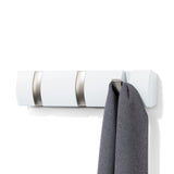 A Flip 3 Hook White wall mounted coat rack from the Umbra range featuring retractable hooks, with a gray towel hanging on it.