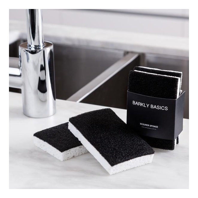 Two black and white scourer sponges resting on the edge of a stainless steel sink