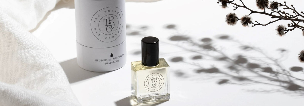 Small perfume oil bottle on a white table beside dried stems
