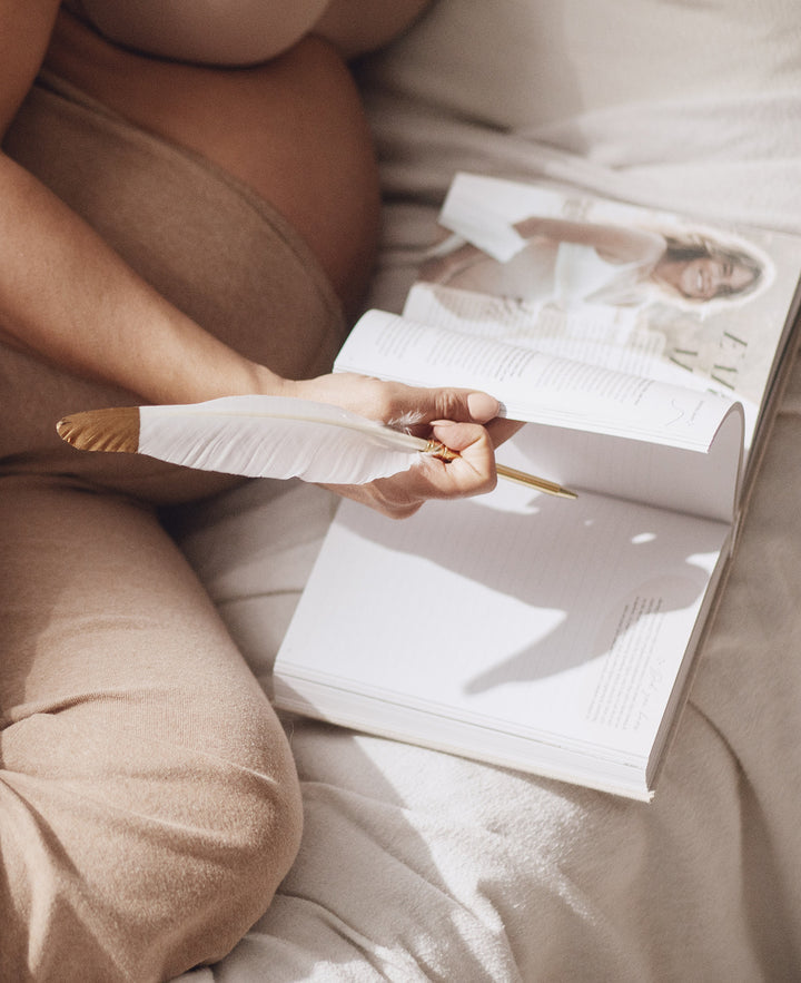 A pregnant woman reading a pregnancy journal on a bed.