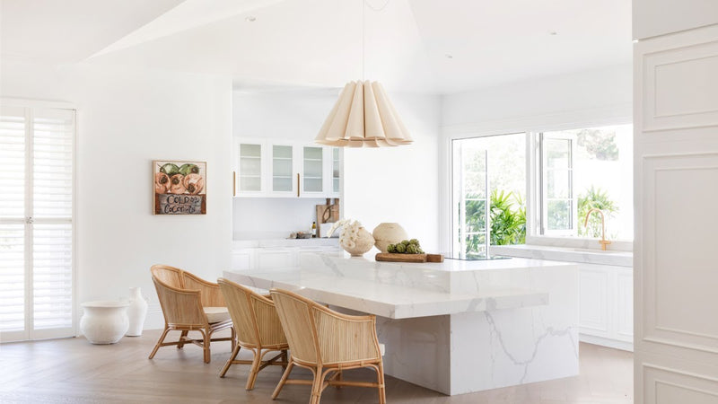 A white kitchen with a wooden table and Three Birds Renovations: Dream Home How-To chairs.