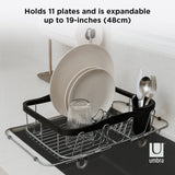 A Sinkin Multi-Use Dish Rack - Black/Nickel by Umbra that holds plates and is adjustable up to 18cm.