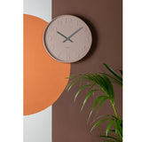 A Karlsson clock enhances the minimal aesthetic of a wall adorned with an orange wall next to a plant.