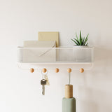 An Umbra wall-mounted Estique Key Hook & Organizer - White / Black featuring hanging hooks for keys and plants in an entryway.
