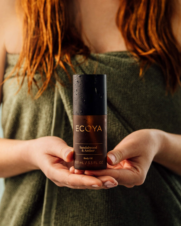 A woman holding a bottle of Ecoya Limited Edition | Sandalwood & Amber Body Oil, showcasing the perfect blend of home fragrance and Scandinavian design.