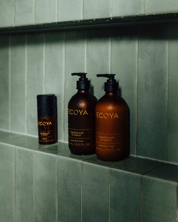 Two bottles of Limited Edition | Sandalwood & Amber Hand & Body Lotion by Ecoya, perfect for scandinavian home design enthusiasts, sit on a green tiled wall.