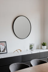 A modern dining room with black chairs and a round Umbra Hub Mirror 45cm Black.