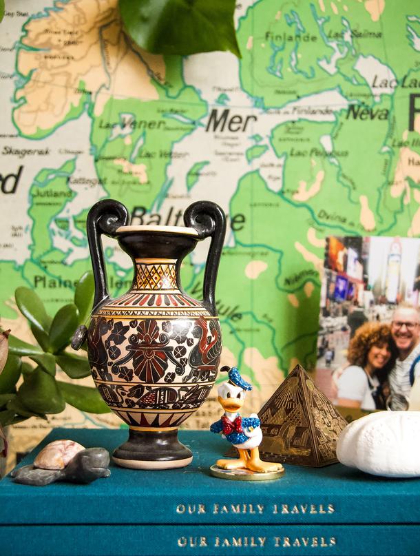 Travel souvenirs, photos and a patterned urn on a stack of teal journals in front of a map