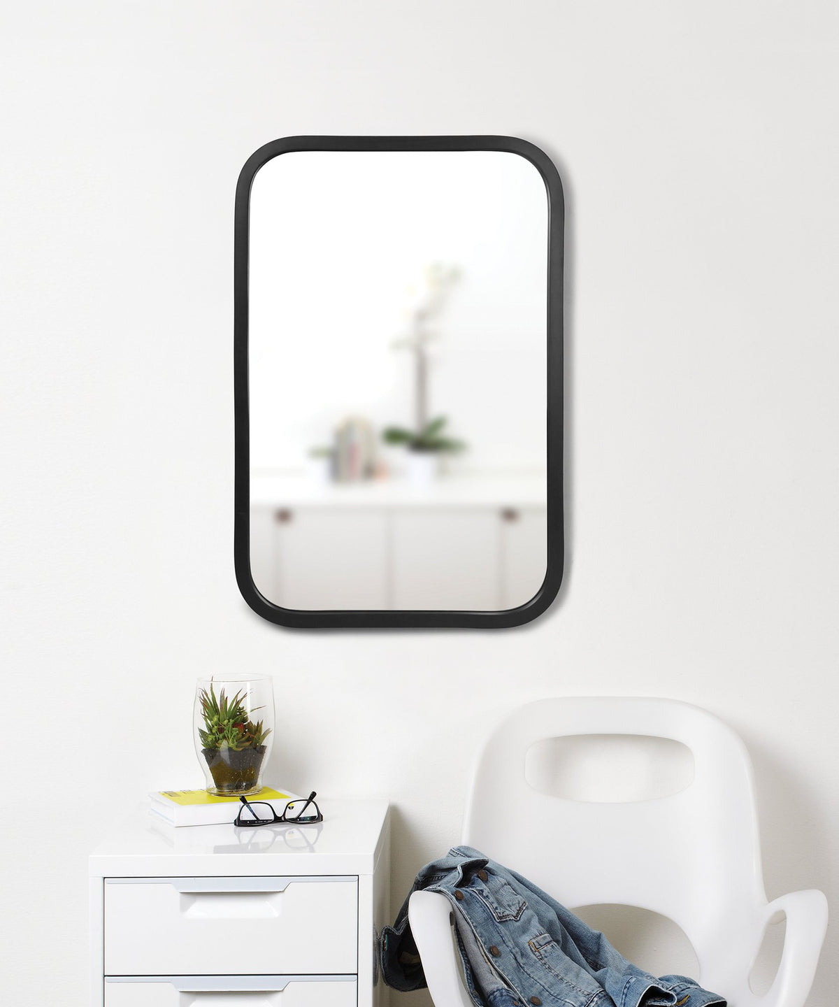 Umbra Hub rectangle mirror in black above a console with a plant and chair