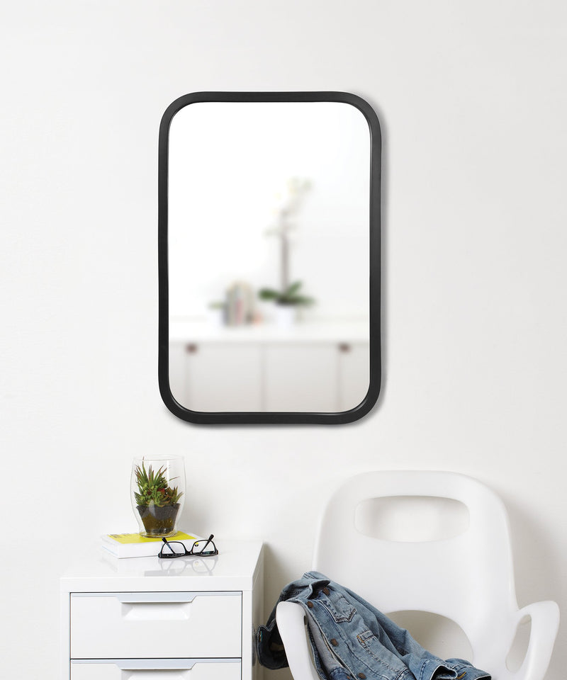 A decorative black mirror, the Umbra Hub Mirror - Rectangle 61X91" Black, hung elegantly on a wall adjacent to a sleek white chair.