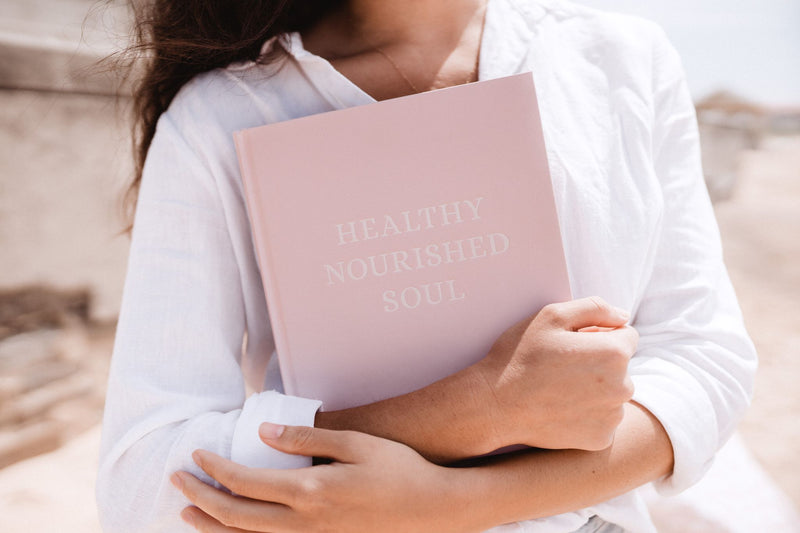 A woman embarks on a wellness journey, holding a Healthy Nourished Soul - Book promoting self-care for a nourished soul published by Epicurean Publishing.