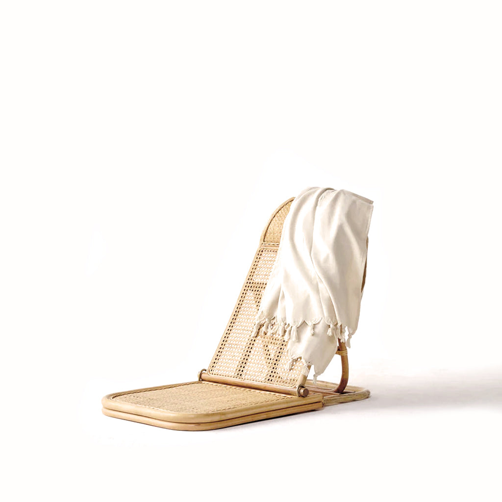A lightweight rattan chair with a quick-dry TURKISH TOWEL – PALM TREE by Brel Club on it.