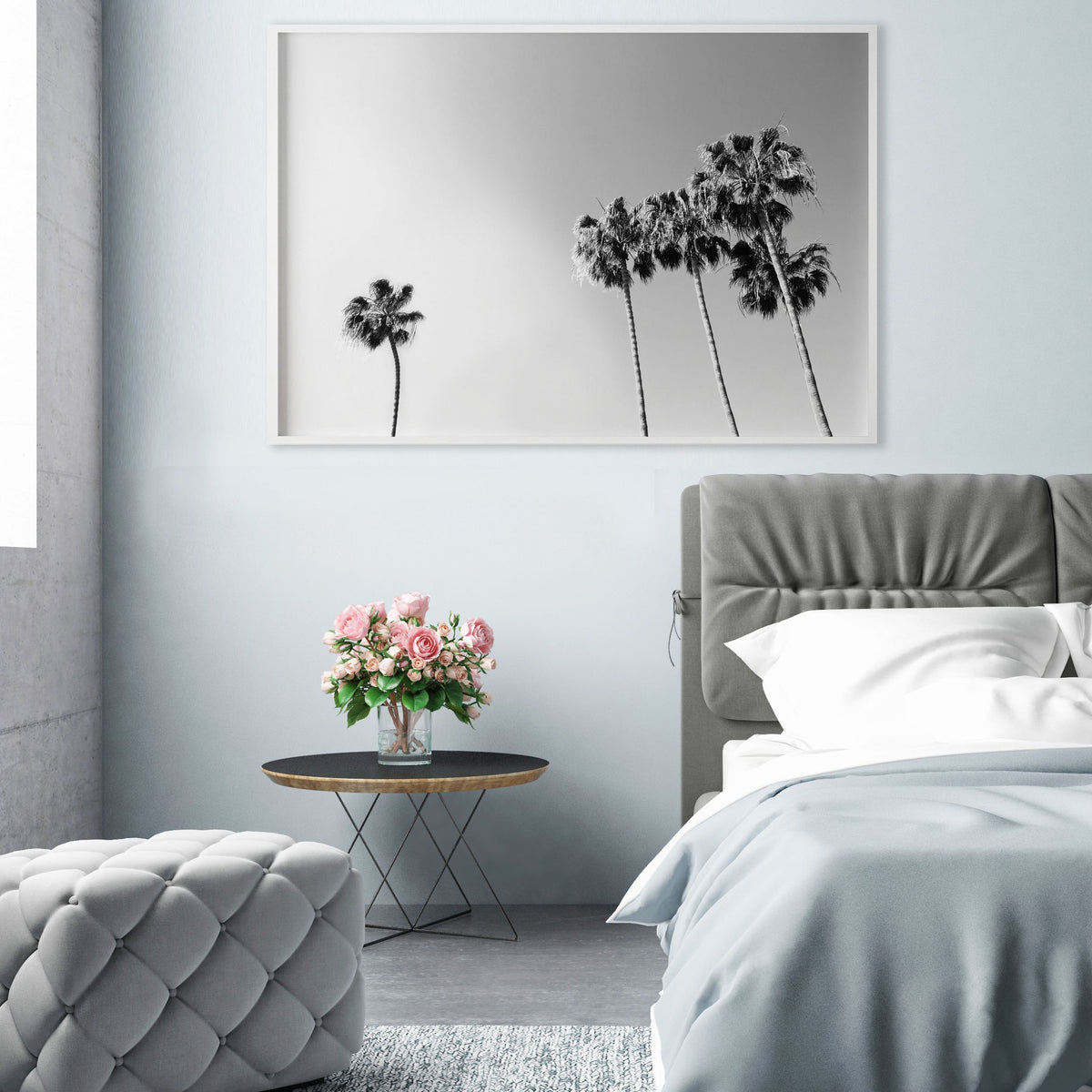 Palm print framed above a grey bed beside a side table with pink flowers