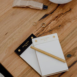 A limited edition Daily notes stationery set showcasing a Papier HQ notepad on a wooden table, accompanied by a refined gold pen.