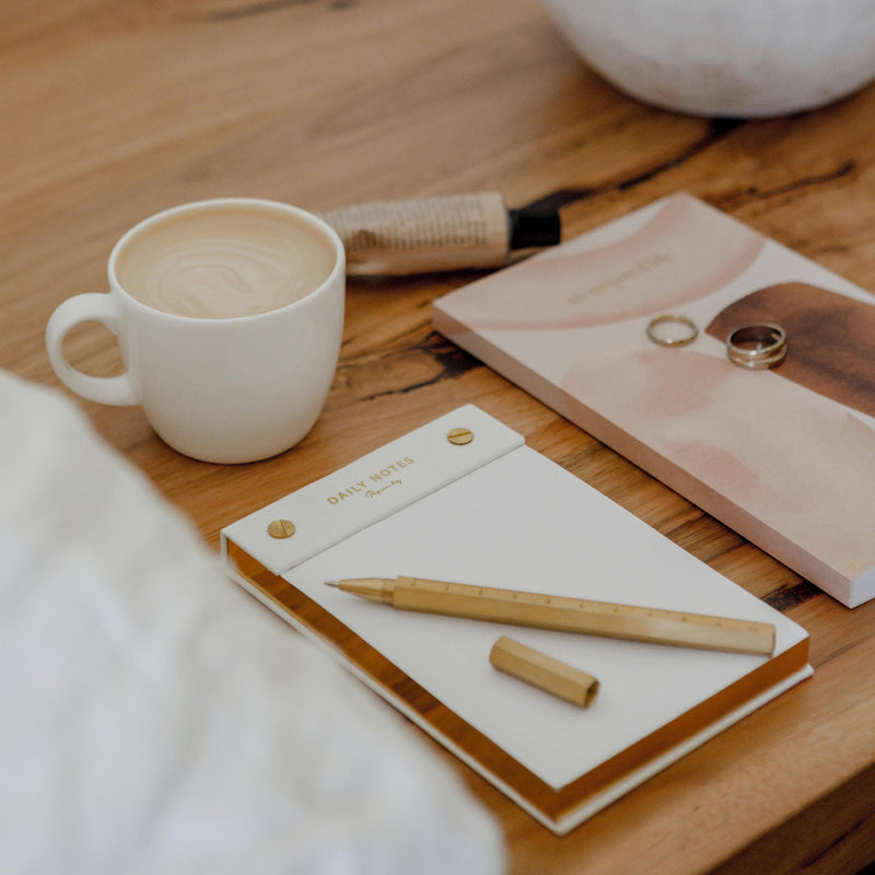 A limited edition Daily notes notebook and pen from Papier HQ, accompanied by a cup of coffee, placed on a wooden table.