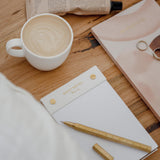 A cup of coffee and a limited edition Papier HQ Daily notes notebook on a bed.