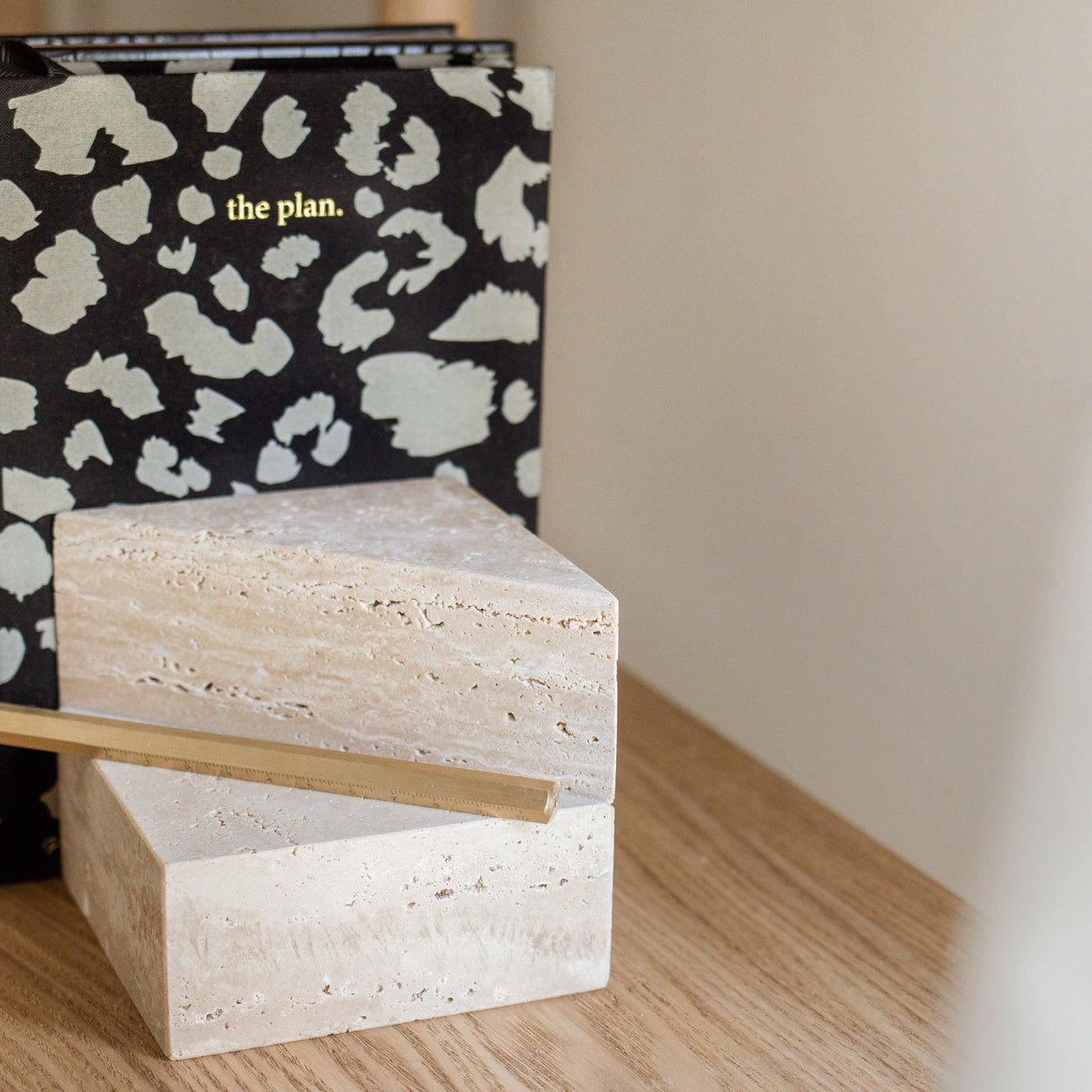 Two stacked travertine bookends on a timber surface with a patterned notebook behind