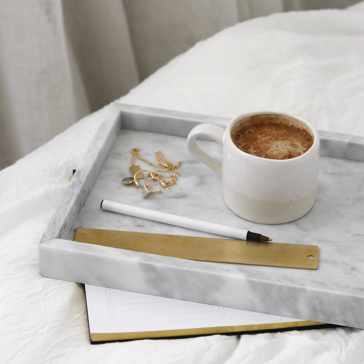 Grey marble tray on a bed holding a coffee cup, pen and small dish