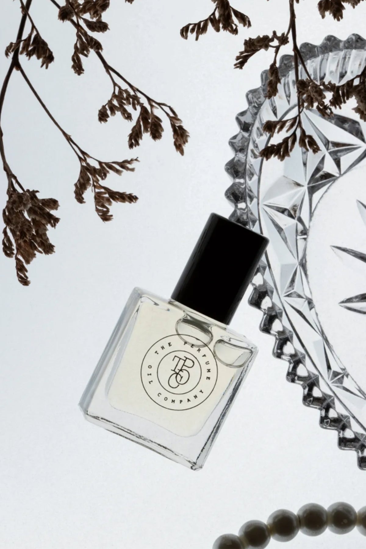 A bottle of LUSH perfume fragrance on a table with pearls, inspired by Be Delicious (DKNY), from The Perfume Oil Company.