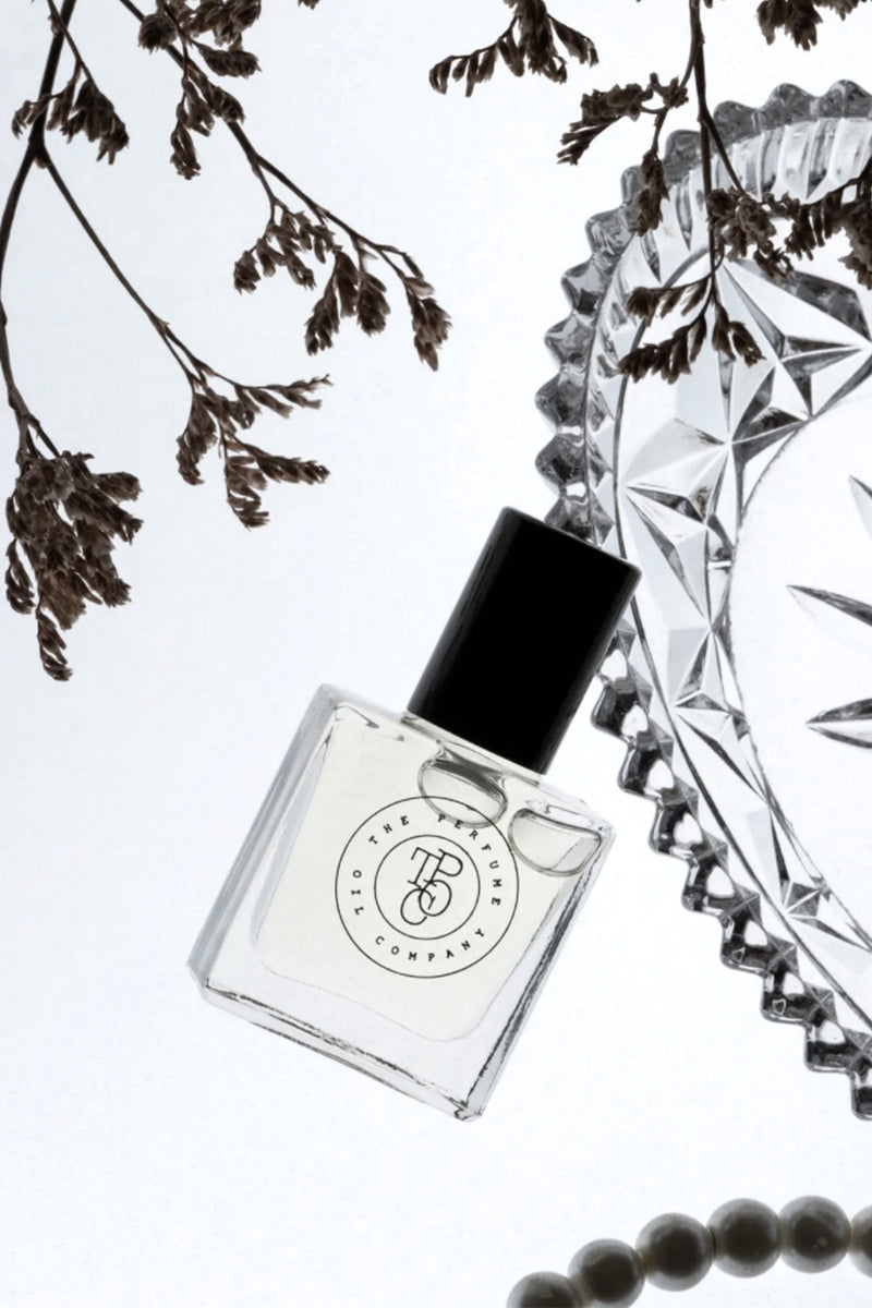 A bottle of The Perfume Oil Collection Gift Set - Fresh from The Perfume Oil Company on a white surface with pearls, branches, and floral fragrances.