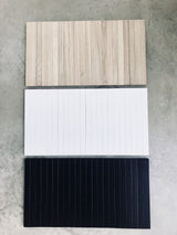 A white, black, and wood panel of the ARM CHAIR SIDE REST by Ned Collections on a concrete floor.