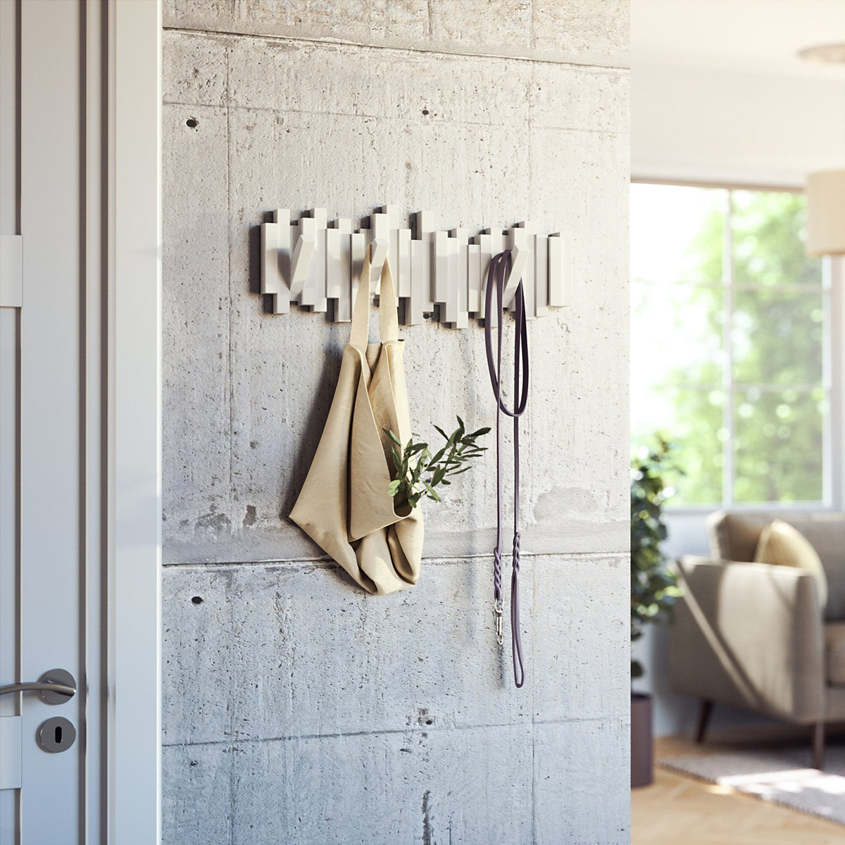 Umbra Sticks multi hook rack in white on a concrete wall holding a coat and bag