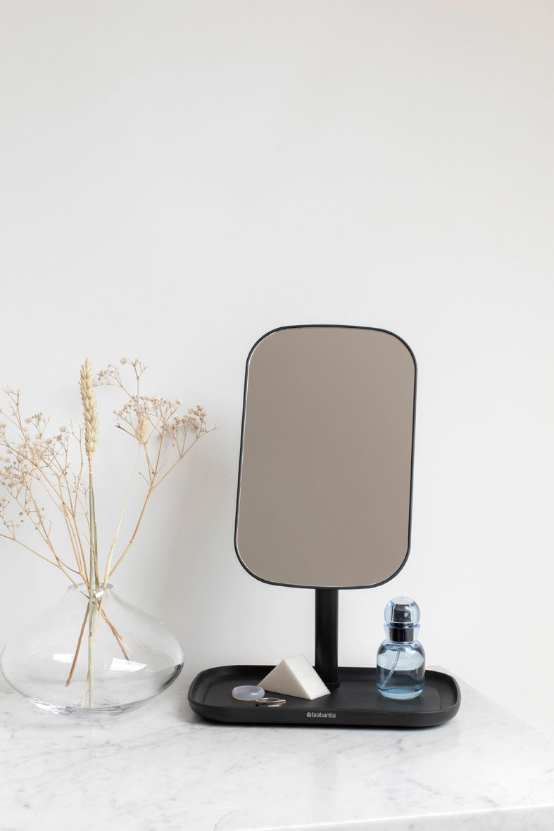 An adjustable Flux Home black mirror with a storage tray on a white counter top.