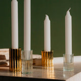 Three Ribb Candle Holder Set - Clear by Zakkia are layered on a table next to a book.