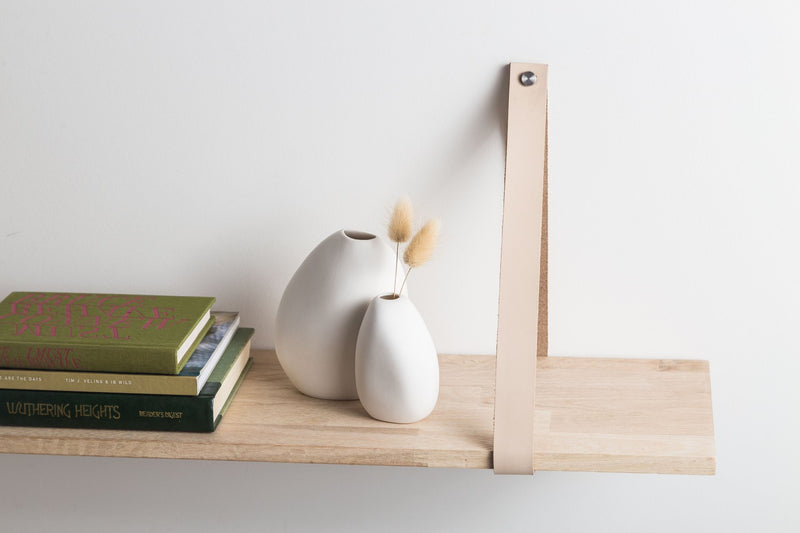 A hand-crafted wooden shelf with a Harmie Vase - Pod - White and books, showcasing organic seed-like shapes by Ned Collections.