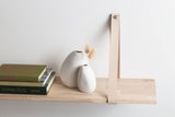 A Vietnamese artisans wooden shelf displaying an exquisite Ned Collections Harmie Vase - Seed Grey alongside a collection of books, all arranged in a manner inspired by organic seed-like shapes.