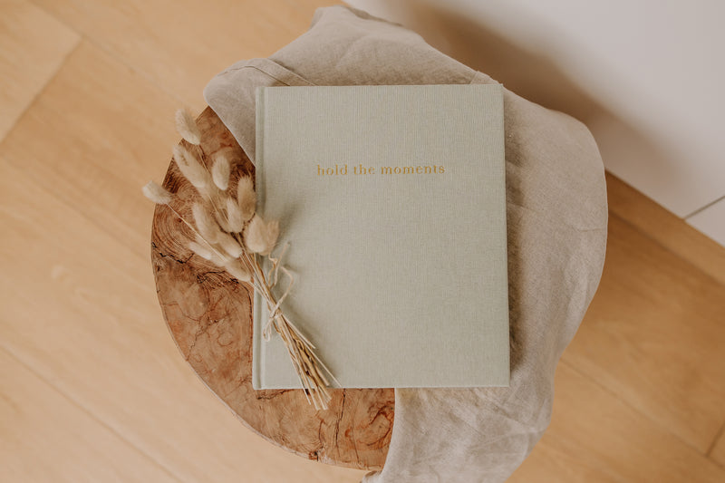 An Olive + Page - Hold The Moments Journal on a wooden table.