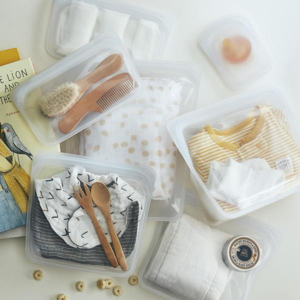 A set of Stasher STAND UP MINI-CLEAR plastic containers with baby clothes and utensils.