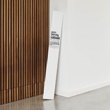 The Stendig Calendar in its branded packaging tube leaning against a timber slat wall, showing the rolled oversized format