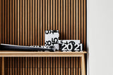 Torn Stendig Calendar pages styled as black and white gift wrap on boxes atop a timber console against a slat wall
