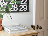 Stendig Calendar hung above a shelf of books and a vase in a minimal room