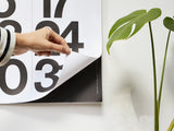 Hand holding the Stendig wall calendar beside a monstera plant