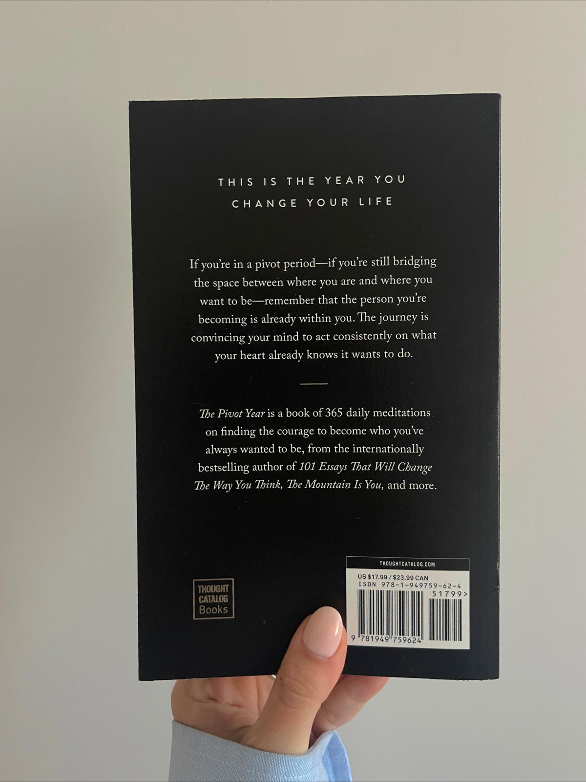 A hand holding up the back cover of The Pivot Year, showing the blurb and barcode