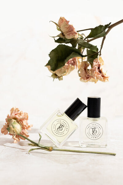 Perfume oil bottles beside a stem of peach flowers on white