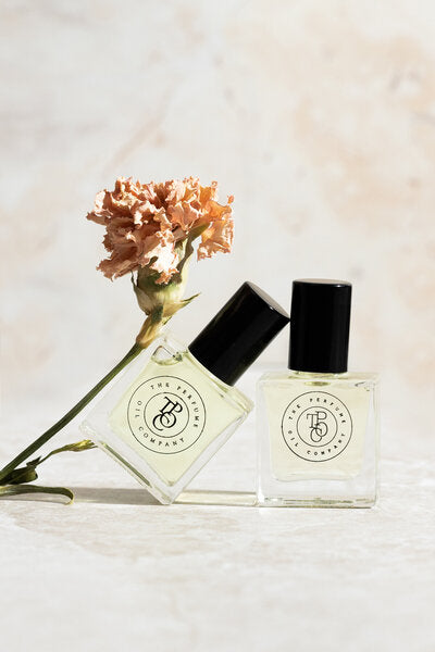 Two bottles of perfume from The Perfume Oil Company's Designer Type Collection, inspired by Wood Sage & Sea Salt (Jo Malone), sitting next to a flower.