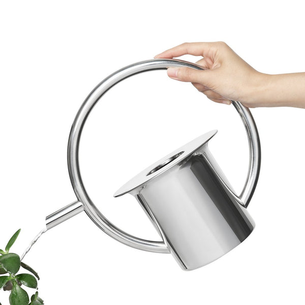 The Quench Watering Can - Stainless Steel from the Umbra range features a 360-degree handle while being used to water a plant.