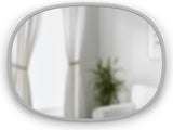 The Umbra Hub Oval Mirror, with its rubber rim, adds a sleek touch to any room. This round mirror effortlessly complements the white couch and potted plant, creating a modern and stylish ambiance.