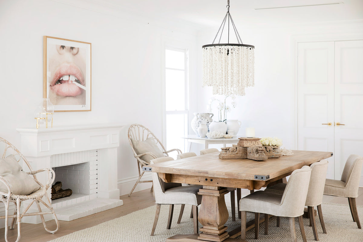 Timber dining table with white chairs, a fireplace and a beaded pendant