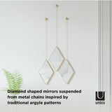 DIMA MIRROR - BRASS, manufactured by Umbra, is a diamond shaped mirror hanging from chains inspired by argyle patterns.