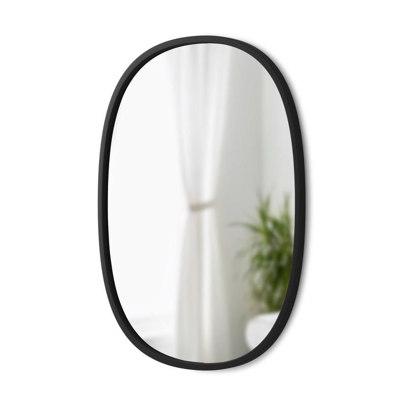 The Hub Mirror Oval - Black, from the Umbra range, features a sleek black frame with a rubber rim, displayed on a white wall.