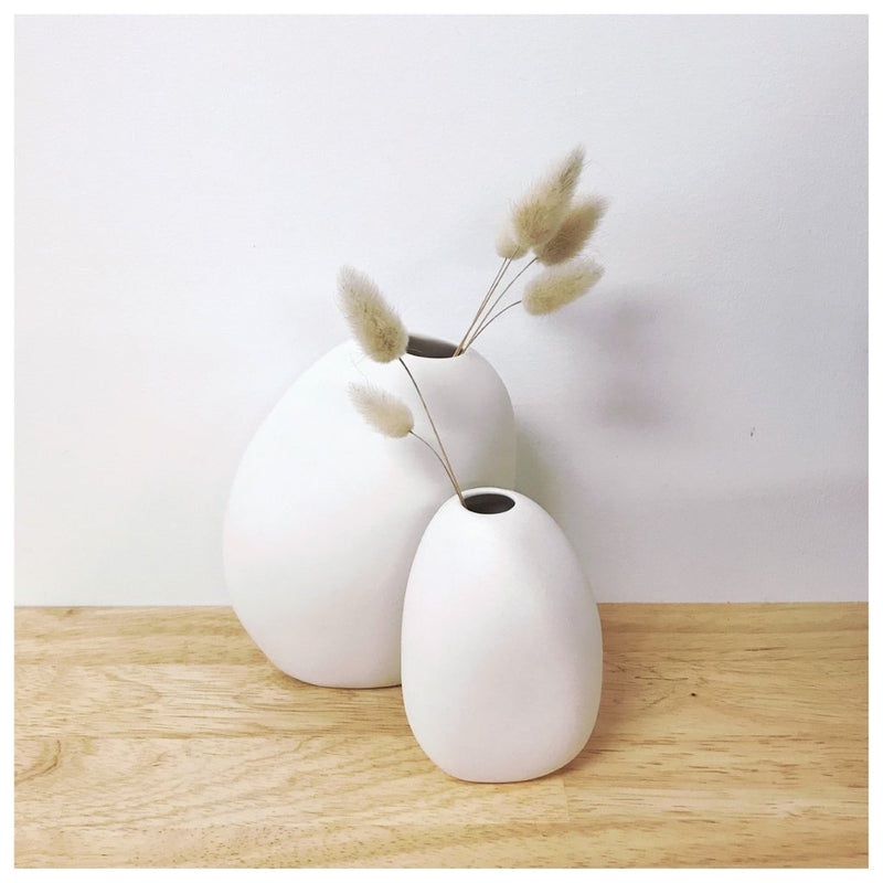 Two white vases, handcrafted by Vietnamese artisans, sitting on a wooden table. These stunning pieces belong to the Ned Collections and include the exquisite Great Harmie Vase - White / Natural.