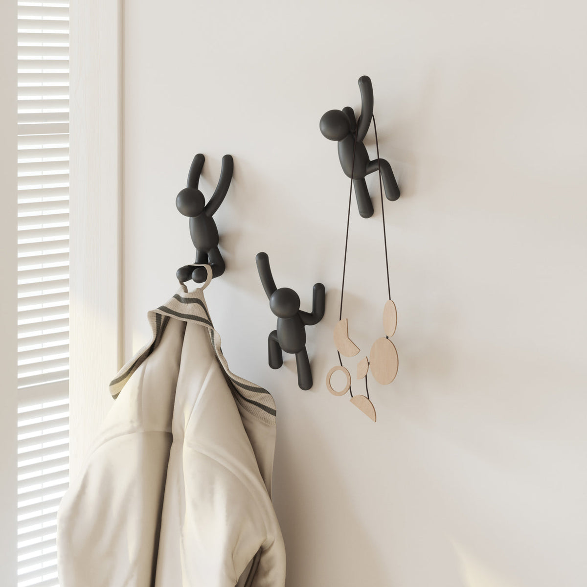 Three black Umbra Buddy Hooks hanging on a coat rack.