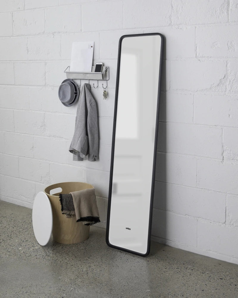 The Umbra range includes a sleek and stylish Umbra HUB LEANING MIRROR - BLACK, designed in black and white, placed gracefully next to the clean white wall.